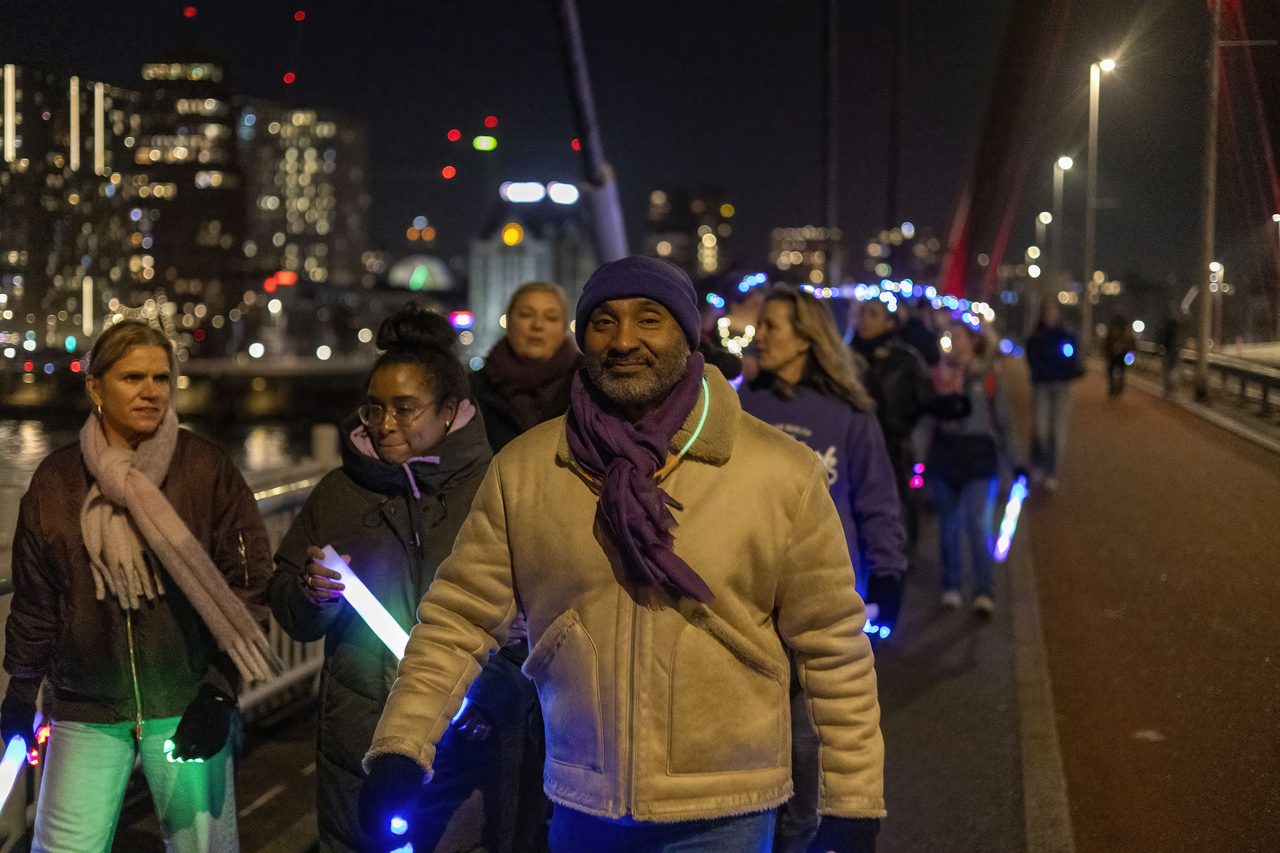 Wandelaars met lichtstaven lopen in het donker over een Rotterdamse brug