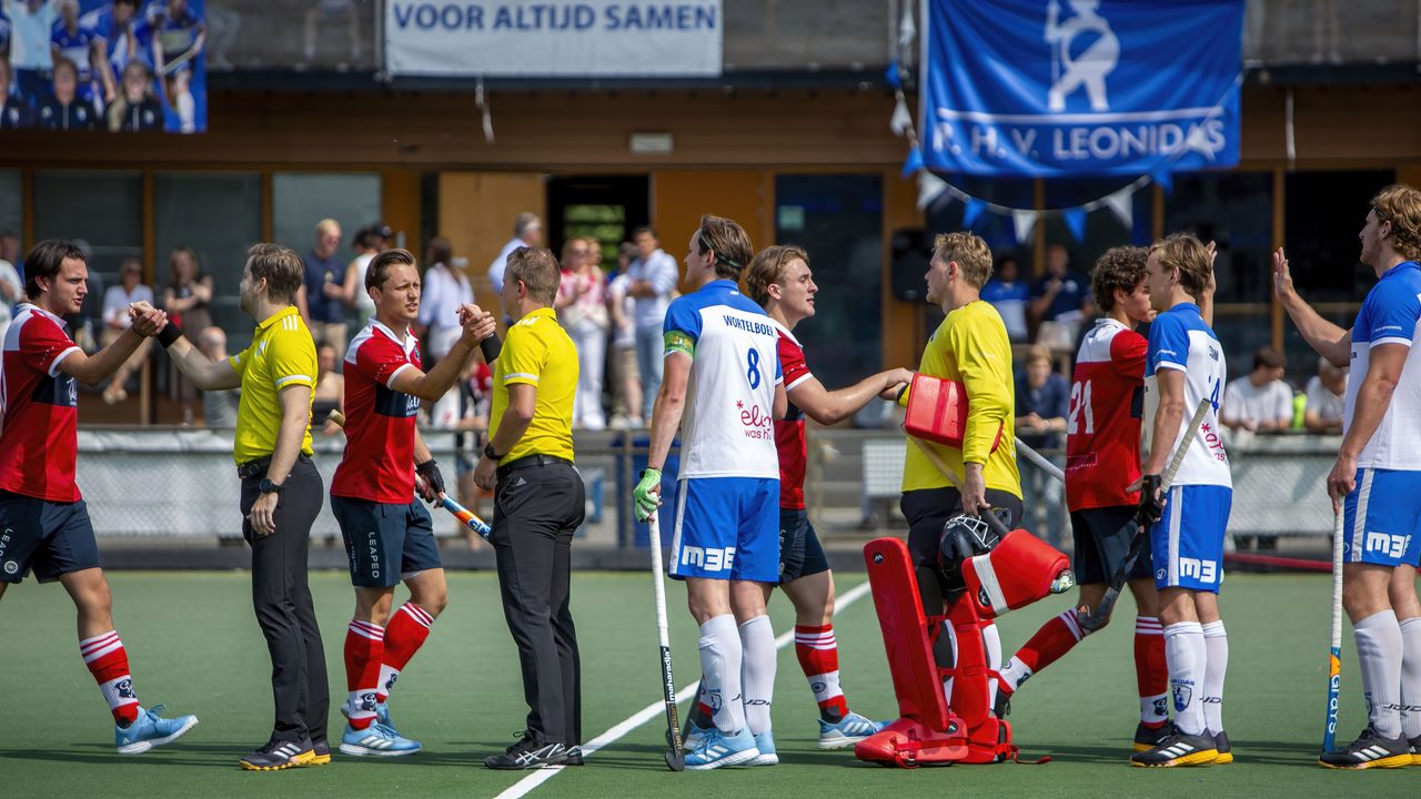 Spelers van Leonidas en de Gooische geven de scheidsrechters een hand onder de clubvlag