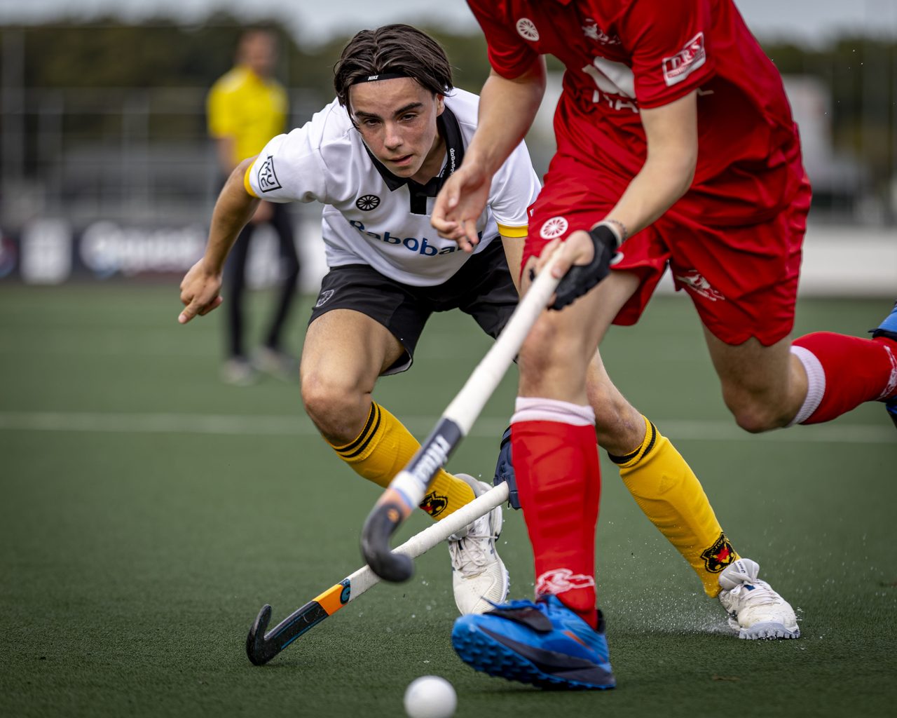Duel om de bal tussen een speler in wit en een speler in rood