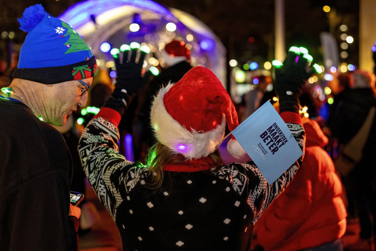 Deelnemer met kerstmuts en een vlaggetje met Onderzoek maakt beter steekt de handen in de lucht