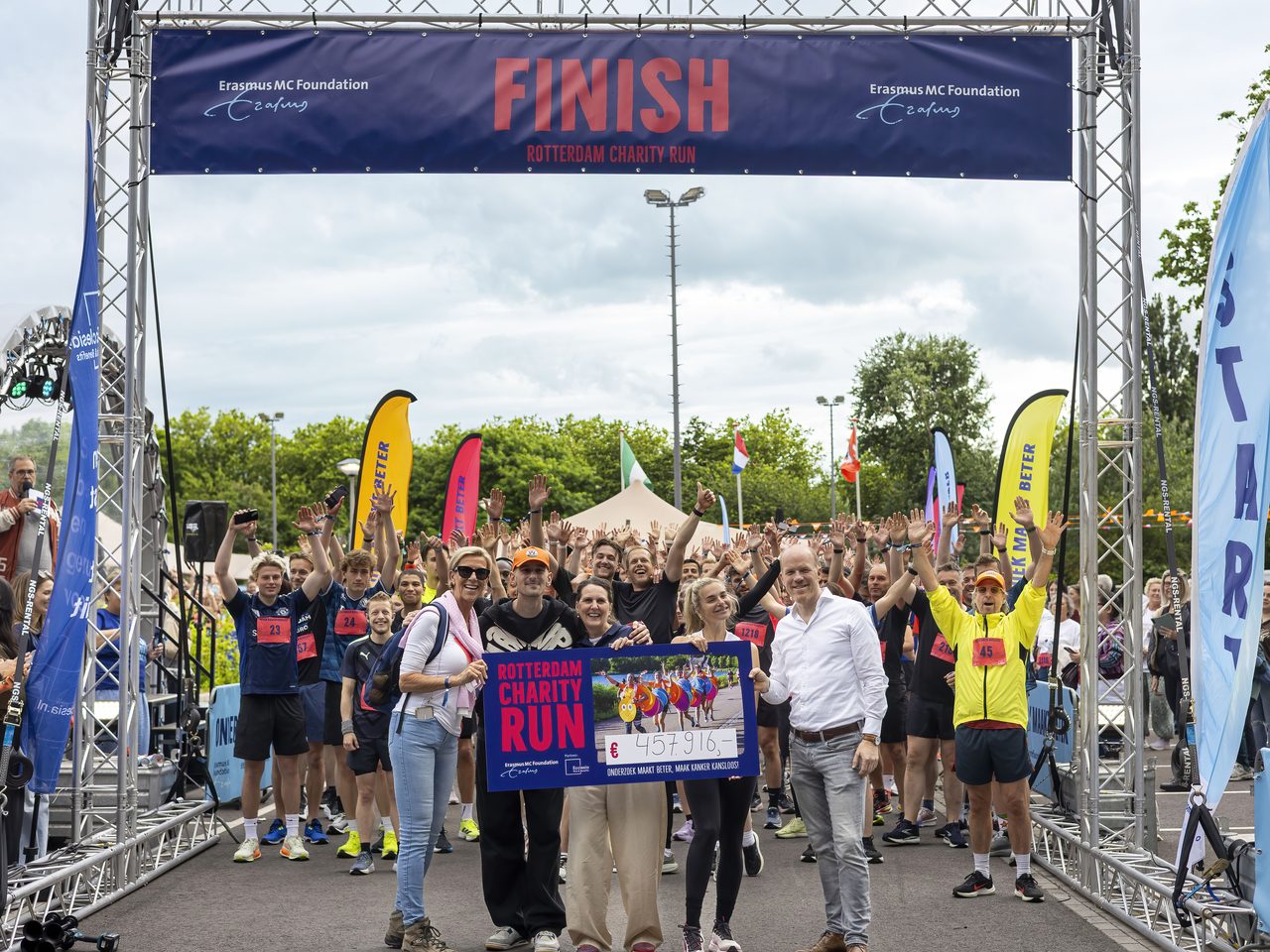Deelnemers en organisatie onder de finishboog van de Rotterdam Charity Run met de cheque