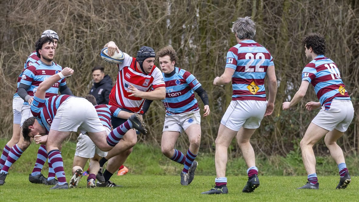 Rugbyspeler in rood-wit breekt met de bal onder de arm door de verdediging