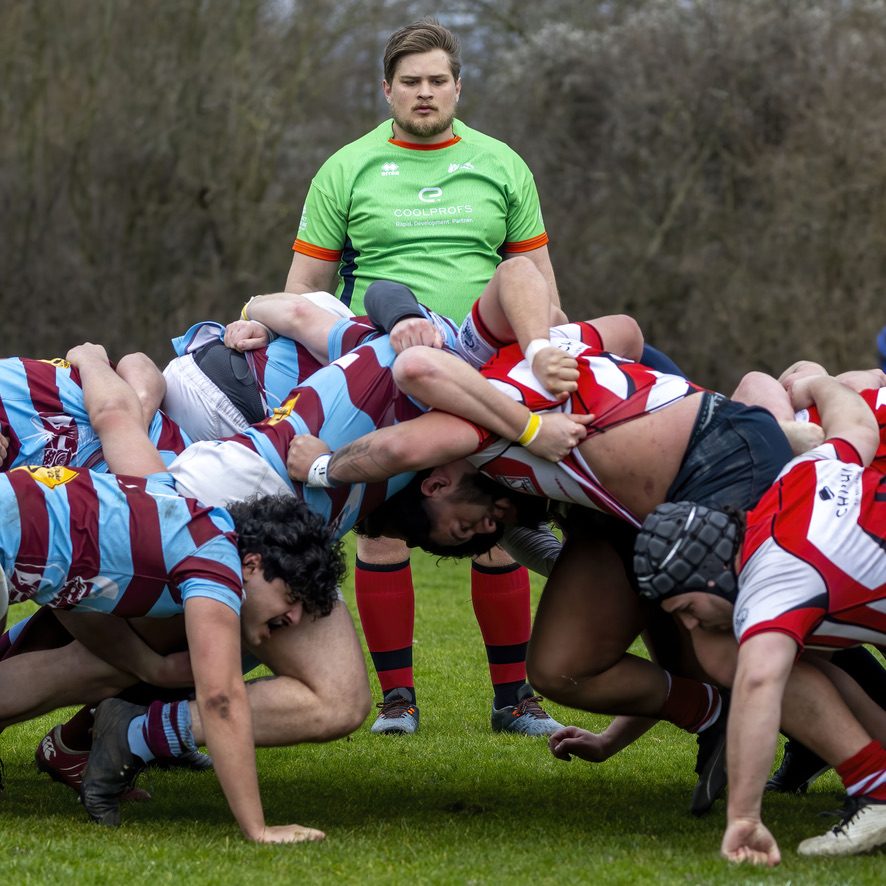 Scheidsrechter kijkt toe terwijl twee rugbypacks tegen elkaar in de scrum zetten
