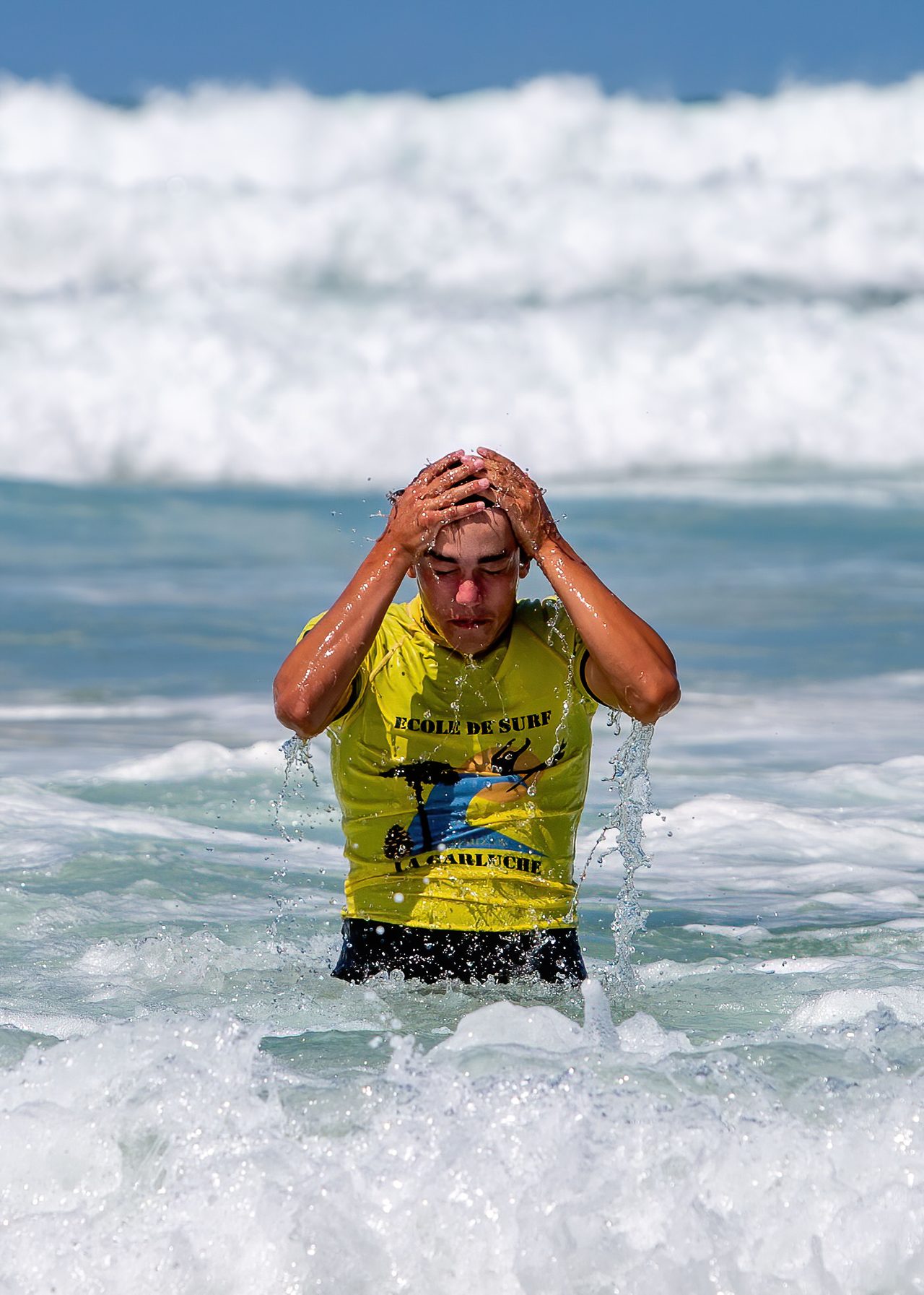 Surfer staat tot zijn middel in zee en strijkt met beide handen het water uit zijn haar