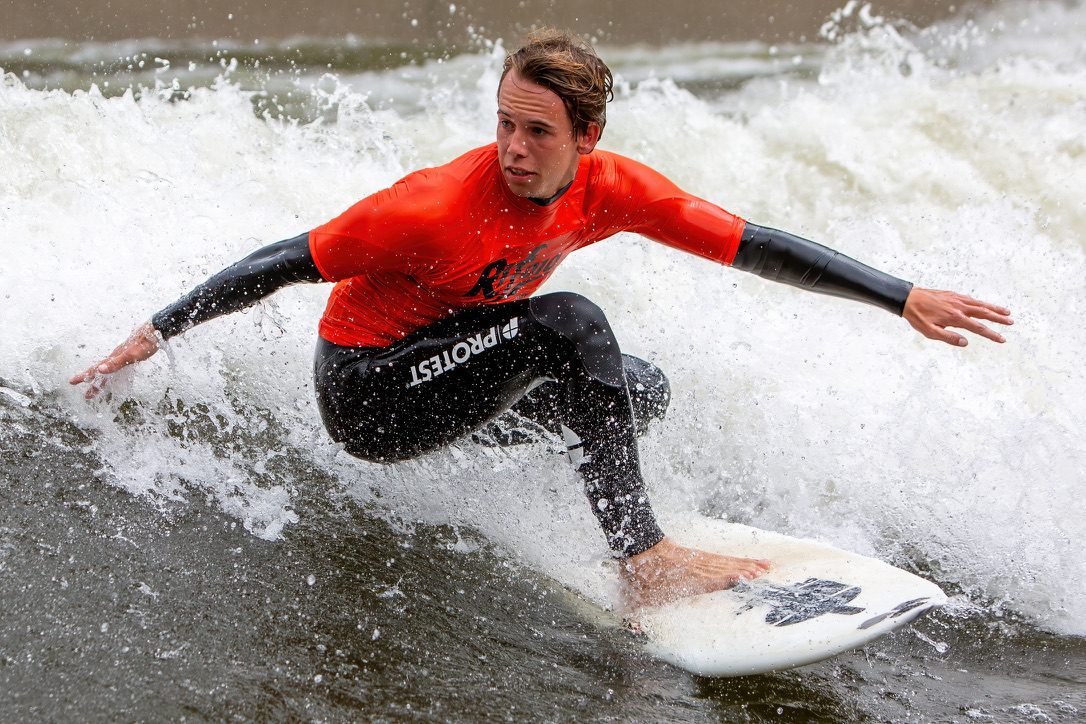 Surfer in oranje shirt maakt een bocht op de golf