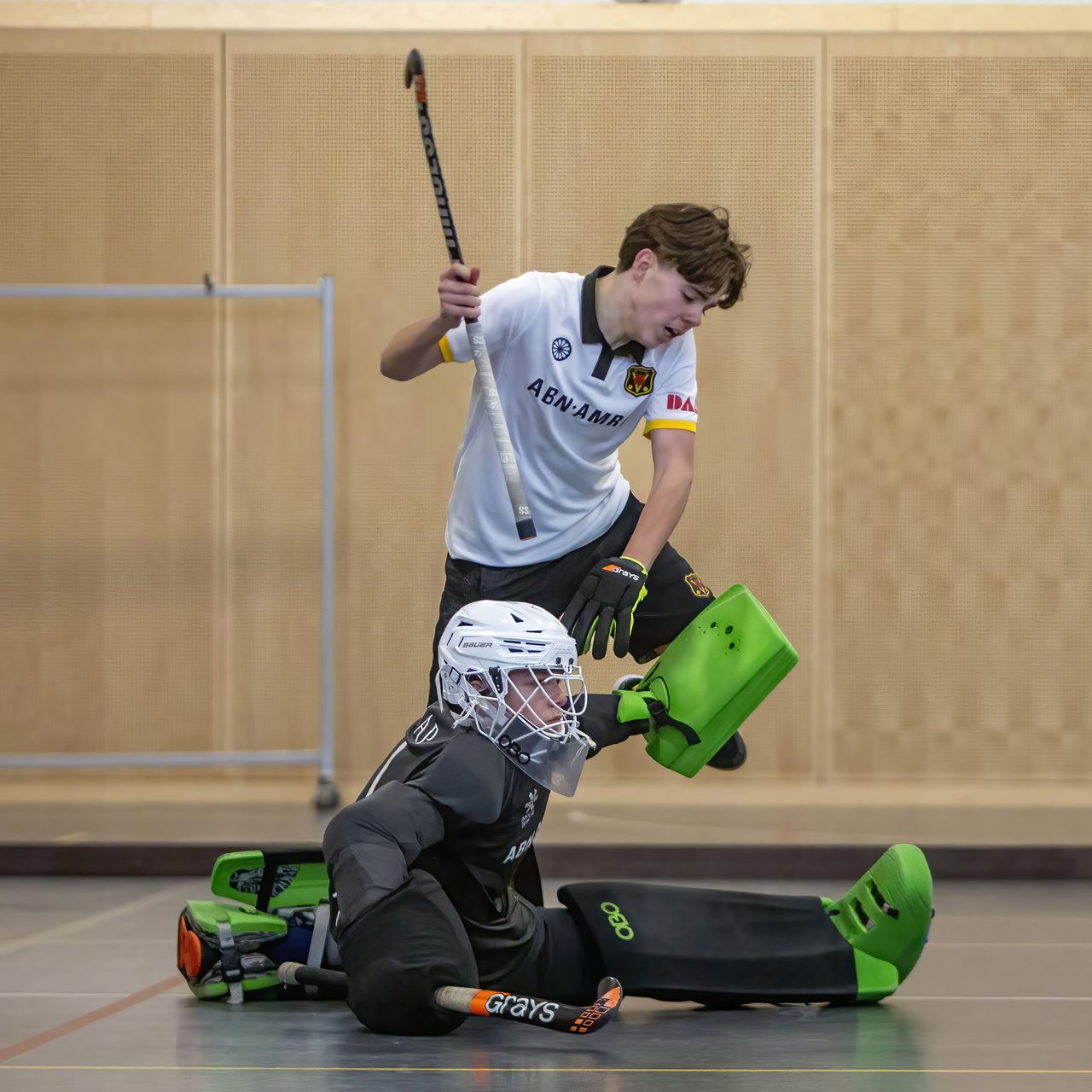 Keeper ligt op de vloer na een redding terwijl een aanvaller zijn stick heft