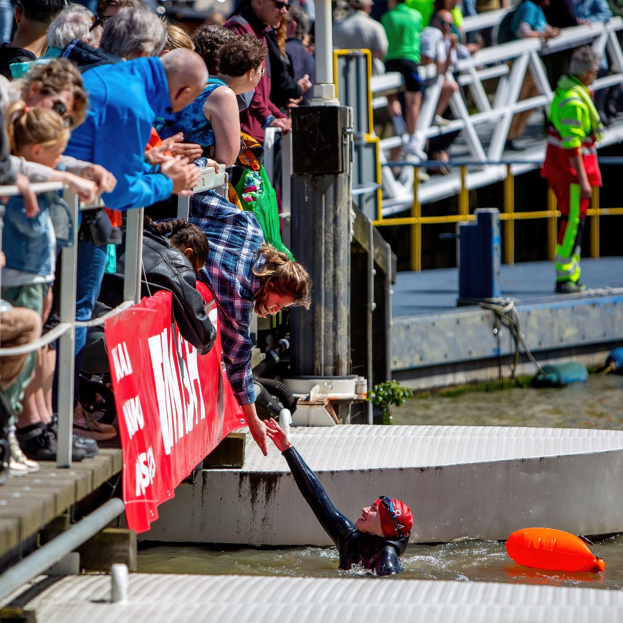 Een zwemmer reikt bij de finish omhoog naar een toeschouwer